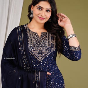 May include: A navy blue kurta with gold embroidery and a matching dupatta. The kurta has a V-neck and three-quarter sleeves. The dupatta is decorated with a border of gold embroidery.