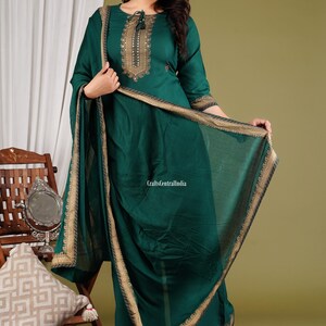 May include: A woman wearing a green kurta with gold embroidery and a matching dupatta. The kurta has a round neckline and three-quarter sleeves. The dupatta has a gold border and is draped over the woman's shoulders.