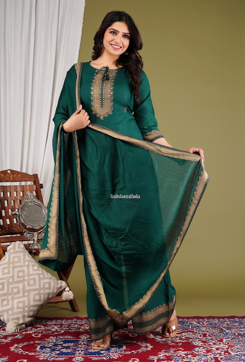 May include: A woman wearing a green kurta with gold embroidery and a matching dupatta. The kurta has a round neckline and three-quarter sleeves. The dupatta has a gold border and is draped over the woman's shoulders.