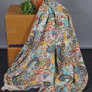 May include: A white kantha quilt with a paisley pattern in shades of blue, green, orange, and red. The quilt is draped over a cardboard box and a terracotta pot.