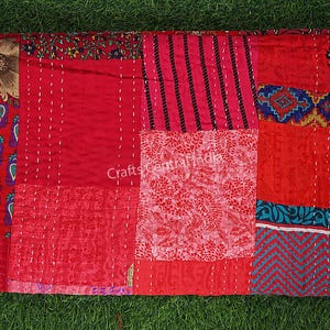 May include: A patchwork quilt with a variety of red fabrics, including floral, paisley, and striped patterns. The quilt is hand-stitched with white thread and features a mix of textures and designs. The quilt is a vibrant and colorful textile.