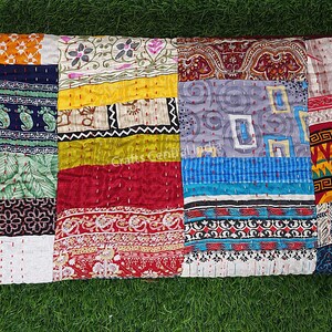 Könnte beinhalten: Ein Patchwork-Quilt mit einer Vielzahl von bunten Stoffquadraten. Der Quilt weist eine Mischung aus Mustern auf, darunter Blumen-, Paisley- und geometrische Designs. Der Quilt ist aus Baumwolle und hat eine genähte Textur. Der Quilt ist rechteckig.