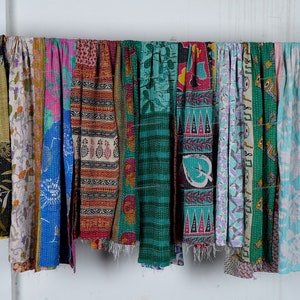 Puede incluir: Una colecci&oacute;n de colchas kantha coloridas, tambi&eacute;n conocidas como colchas de punto kantha, colgadas en una pared blanca. Las colchas est&aacute;n hechas de saris reciclados y presentan una variedad de patrones y colores, incluyendo azul, verde, rosa y rojo.