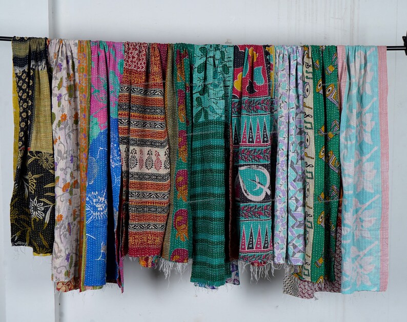 Puede incluir: Una colecci&oacute;n de colchas kantha coloridas, tambi&eacute;n conocidas como colchas de punto kantha, colgadas en una pared blanca. Las colchas est&aacute;n hechas de saris reciclados y presentan una variedad de patrones y colores, incluyendo azul, verde, rosa y rojo.