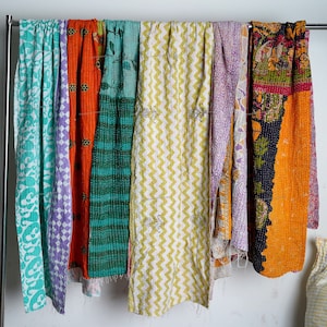 Puede incluir: Siete colchas kantha coloridas colgadas en un estante. Las colchas est&aacute;n hechas de tela de retazos y tienen diferentes patrones, incluyendo florales, geom&eacute;tricos y paisley. Las colchas son todas en varios tonos de azul, verde, amarillo, naranja y morado.