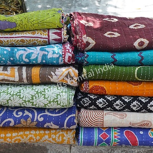 May include: A stack of colorful kantha quilts with various patterns and designs. The quilts are made of recycled saris and are hand-stitched. The quilts are folded and stacked on top of each other. The quilts are a popular choice for home decor and are often used as throws or bedspreads.