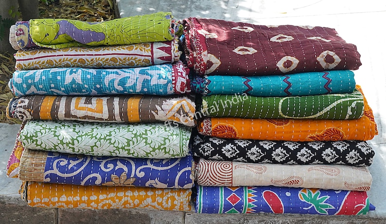 May include: A stack of colorful kantha quilts with various patterns and designs. The quilts are made of recycled saris and are hand-stitched. The quilts are folded and stacked on top of each other. The quilts are a popular choice for home decor and are often used as throws or bedspreads.