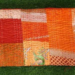 May include: A patchwork quilt made from colorful fabric scraps in shades of orange, red, and brown. The quilt is hand-stitched with white thread and has a unique, rustic look. The quilt is labeled "Crafts Central India".