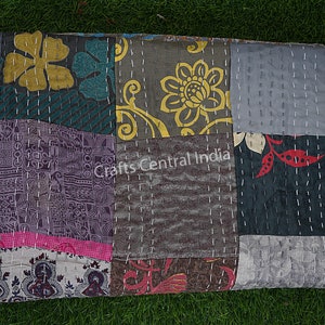 May include: A patchwork quilt with a variety of floral and geometric patterns in shades of gray, blue, pink, yellow, and red. The quilt is made of recycled saris and is hand-stitched with white thread. "Crafts Central India" is printed on the quilt.