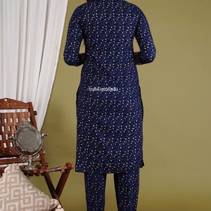 May include: A navy blue printed kurta and palazzo set with gold accents. The set features a floral print and a round neckline. The model is wearing the set and standing on a red patterned rug.