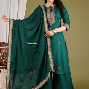 May include: A teal green kurta with gold embroidery and a matching dupatta. The kurta has a round neckline and three-quarter sleeves. The dupatta has a gold border and is draped over the shoulder. The outfit is perfect for a special occasion.