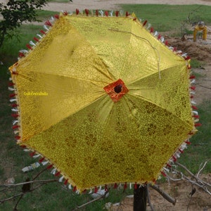 May include: A yellow umbrella with a floral pattern and red trim. The umbrella has a tassel fringe around the edge.