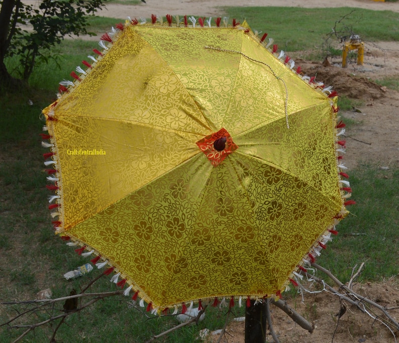 May include: A yellow umbrella with a floral pattern and red trim. The umbrella has a tassel fringe around the edge.