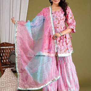 Op de afbeelding: Een roze en blauwe bedrukte jurk met een bijpassende dupatta. De jurk heeft een bloemenprint en een zwierige rok. De dupatta is doorschijnend en heeft een zilveren rand. De jurk wordt gedragen door een vrouw met lang donker haar. De tekst "CraftsCentralIndia" is zichtbaar in de afbeelding.