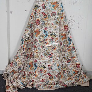 May include: A white kantha quilt with a colorful floral and paisley pattern. The quilt is made of cotton and is hand-stitched. The quilt is folded and displayed on a white surface. "Crafts Central India" is printed on the quilt.