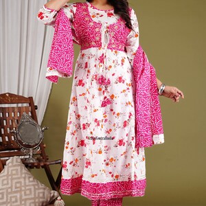 May include: A white floral print kurta with a pink dupatta and matching pants. The kurta has a pink embroidered neckline and a tie-up detail at the waist. The dupatta has a white polka dot pattern.