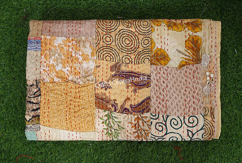 May include: A patchwork quilt made from various fabrics in shades of beige, brown, and gold. The quilt is made up of squares and rectangles of different sizes and patterns, including floral, paisley, and geometric designs. The quilt is hand-stitched and has a rustic, vintage look.