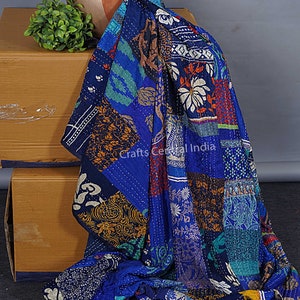 Könnte beinhalten: Eine blaue Kantha-Steppdecke mit Patchwork-Muster, das verschiedene florale und geometrische Muster zeigt. Die Steppdecke ist aus recycelten Saris gefertigt und handgenäht. Die Steppdecke ist über eine Kiste und einen Tontopf mit einer grünen Pflanze drapiert.