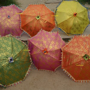May include: Six colorful umbrellas with gold accents and fringe trim. The umbrellas are arranged in a semi-circle on a brown surface.