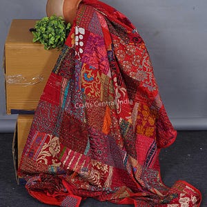 Könnte beinhalten: Ein Patchwork-Quilt in Rot-, Burgunder- und Goldtönen. Der Quilt besteht aus verschiedenen Stoffstücken mit floralen und geometrischen Mustern. Der Quilt ist über einer Pappschachtel und einem Terrakottatopf drapiert.