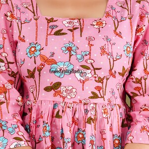 Op de afbeelding: Een roze katoenen jurk met een vierkante halslijn en een bloemenprint. De jurk heeft een geplooide rok en driekwart mouwen.