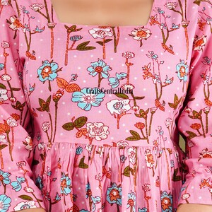 Op de afbeelding: Een roze katoenen jurk met een vierkante halslijn en een bloemenprint. De jurk heeft een geplooide rok en 3/4 mouwen.