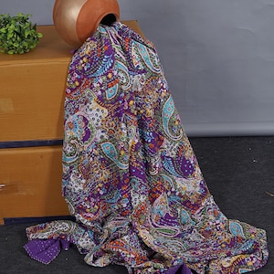 Può includere: Una trapunta in cotone viola caratterizzata da un vivace motivo paisley multicolore con complessi disegni floreali e geometrici. Il tessuto presenta un design denso e ripetitivo nei toni dell'arancione, ottanio, giallo e bianco, con cuciture a vista.