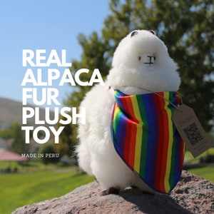 K&ouml;nnte beinhalten: Ein wei&szlig;es Pl&uuml;schtier-Alpaka, das ein Regenbogen-Bandana tr&auml;gt. Das Alpaka ist aus echtem Alpaka-Fell gefertigt und hat ein QR-Code-Etikett mit der Aufschrift "Real Alpaca Fur Plush Toy" und "Made in Peru".