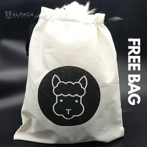 K&ouml;nnte beinhalten: Eine wei&szlig;e Baumwoll-Kordeltasche mit schwarzen Griffen und einem schwarzen Kreislogo mit einer wei&szlig;en Umrandung eines Alpaka-Gesichts. Die Tasche hat den Text "FREE BAG" auf der Seite.