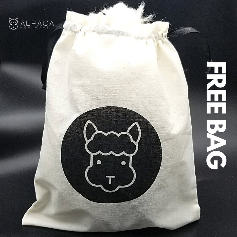 K&ouml;nnte beinhalten: Eine wei&szlig;e Baumwoll-Kordeltasche mit schwarzen Griffen und einem schwarzen Kreislogo mit einer wei&szlig;en Umrandung eines Alpaka-Gesichts. Die Tasche hat den Text "FREE BAG" auf der Seite.