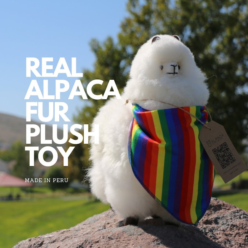 K&ouml;nnte beinhalten: Ein wei&szlig;es Pl&uuml;schtier-Alpaka, das ein Regenbogen-Bandana tr&auml;gt. Das Alpaka ist aus echtem Alpaka-Fell gefertigt und hat ein QR-Code-Etikett mit der Aufschrift "Real Alpaca Fur Plush Toy" und "Made in Peru".