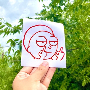 Puede incluir: Una pegatina de vinilo roja que representa a un personaje de dibujos animados haciendo un gesto obsceno. El personaje tiene una expresi&oacute;n de mal humor y el contorno es rojo. La pegatina se sostiene sobre un fondo de follaje verde y un cielo nublado.