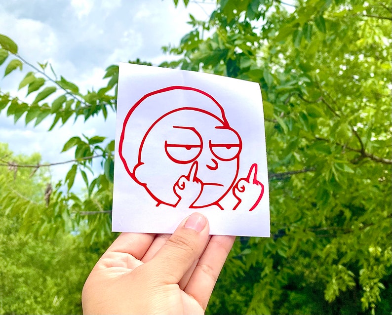 Puede incluir: Una pegatina de vinilo roja que representa a un personaje de dibujos animados haciendo un gesto obsceno. El personaje tiene una expresi&oacute;n de mal humor y el contorno es rojo. La pegatina se sostiene sobre un fondo de follaje verde y un cielo nublado.