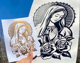 Puede incluir: Dos calcomanías con una imagen religiosa de una mujer con un halo, manos rezando y rosas. Una calcomanía es dorada, la otra es en blanco y negro. El fondo es un cielo azul claro.