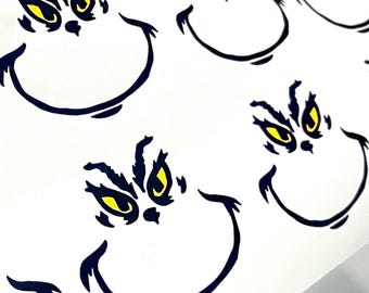 Puede incluir: Una hoja de papel blanco con varias caras de Grinch negras y amarillas impresas en ella. Las caras del Grinch tienen una expresión traviesa con ojos grandes y una gran sonrisa.