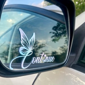 May include: A car mirror with a butterfly decal and the word "Continue" in a cursive font. The butterfly is white with a gradient of blue and purple. The text is also white with a gradient.