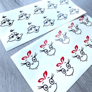 May include: Sheets of white stickers featuring cartoon faces. Some stickers have a simple face design, while others include red bows. The faces have black outlines and are smiling.