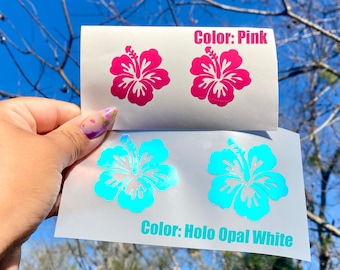 May include: Two sheets of stickers featuring hibiscus flower designs. One sheet displays two pink flowers with the text "Color: Pink." The other sheet shows two turquoise flowers with the text "Color: Holo Opal White."