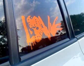 May include: Orange vinyl decal on a car window. The decal features the word "LOVE" with the letter "O" replaced by a hockey mask design. The decal has a dripping effect.