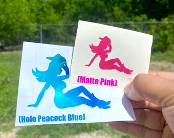 May include: Two stickers featuring a silhouette of a woman in a cowboy hat and boots. One sticker is holo peacock blue, and the other is matte pink. The text on the stickers reads "(Holo Peacock Blue)" and "(Matte Pink)".