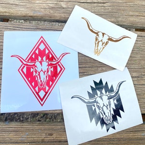 May include: Three white stickers with bull skull designs. One sticker features a red bull skull inside a red diamond shape. Another has a gold bull skull. The third sticker has a black bull skull with a black and white geometric pattern.