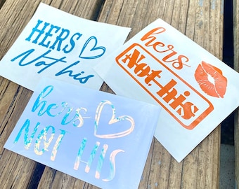 May include: Three white stickers with the phrases "HERS Not his" in various fonts and colors. One sticker has a blue script, another has orange text with a kiss graphic, and the third has iridescent text.