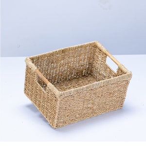 May include: A rectangular woven seagrass basket with two wooden handles. The basket is empty and has a natural beige color.