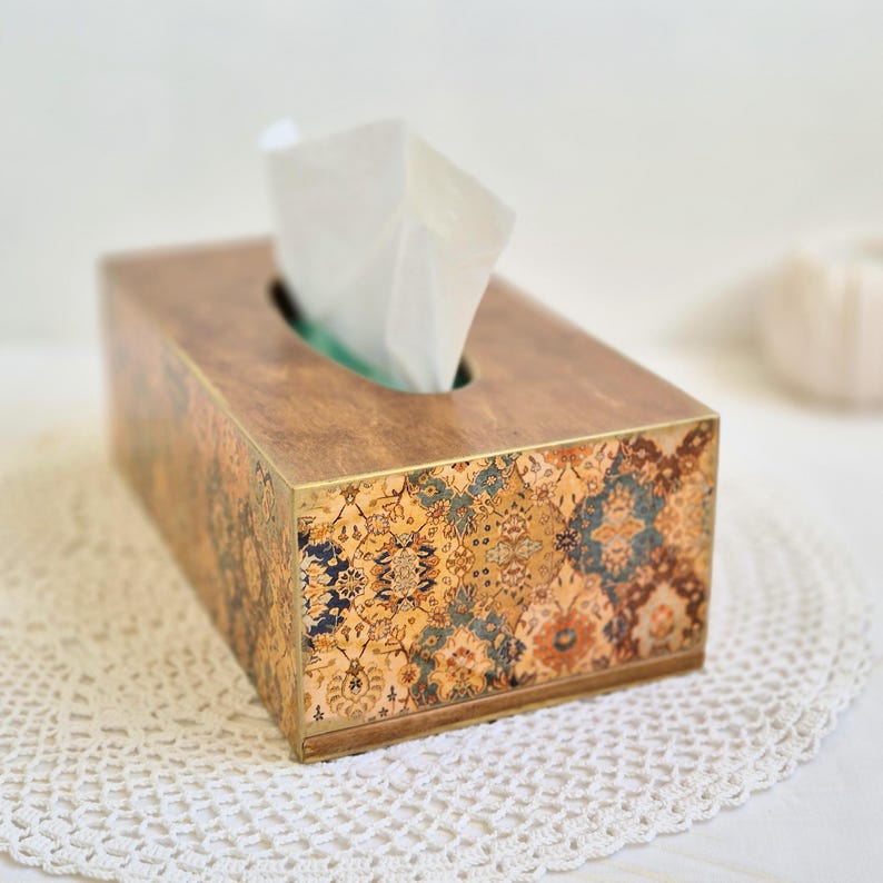 Pu&ograve; includere: Un porta fazzoletti in legno con un design decorativo a motivi in ​​oro, blu e verde. La scatola ha un bordo in ottone e una fessura per i fazzoletti.