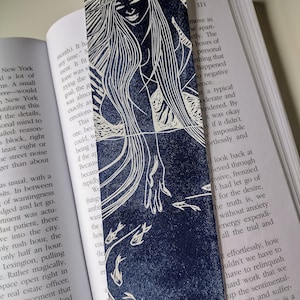 May include: A blue and white bookmark with a woman's silhouette and a design of fish swimming in a circle. The bookmark has the text "move in the apartment" on the right side.