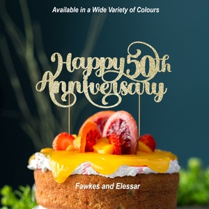 May include: Gold glitter cake topper with the text "Happy 50th Anniversary" on a cake decorated with fruit and yellow frosting. The cake is labelled "Fawkes and Elssar".