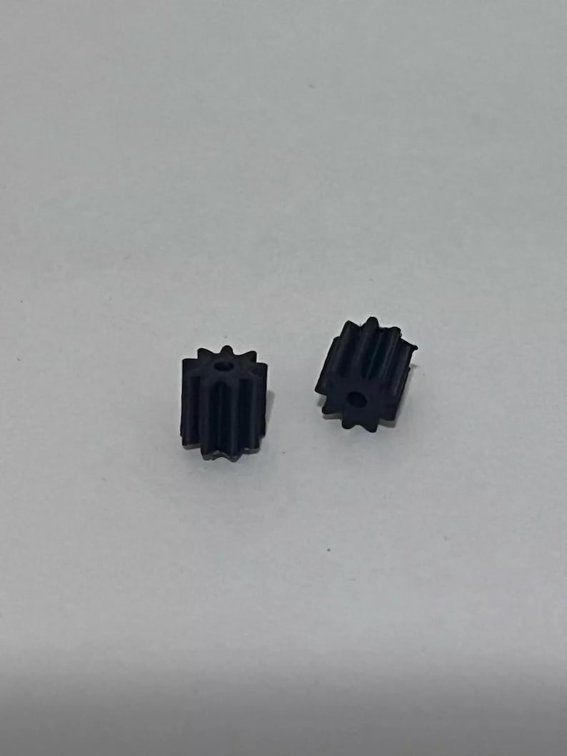 Może przedstawiać: Dwa małe czarne plastikowe koła zębate.