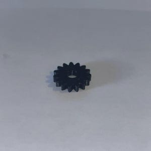 May include: A small, black, circular gear featuring twelve evenly spaced teeth around its perimeter and a single, centred circular hole. The component is constructed from a solid, dark material with a smooth finish and a uniform, symmetrical design.