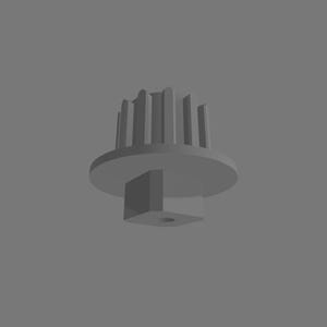 Puede incluir: Un componente de engranaje de pl&aacute;stico gris con una base circular, una serie de crestas verticales a lo largo del borde superior y una protuberancia cuadrada que se extiende desde el centro inferior, con un peque&ntilde;o orificio circular.
