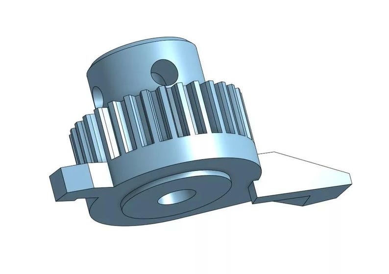 May include: A silver-colored metal gear with a toothed edge and a small hole in the center. The gear is attached to a smaller, flat piece of metal with a rounded edge.